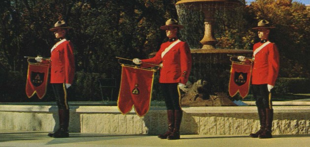 This is an image of three royal guards. They are wearing red blazers, black pants, and brown boots. They are holding flags and wearing brimmed hats.