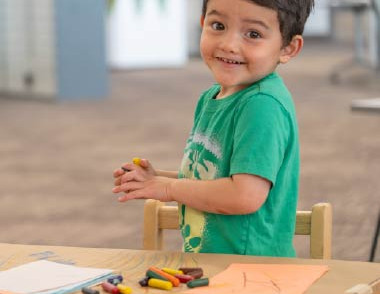 Child standing beside a table with crayons and a drawing activity.
