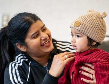 Adult helping a toddler wearing a knit hat during a library visit.