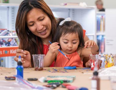 Adult and child painting together at a craft table in a library.