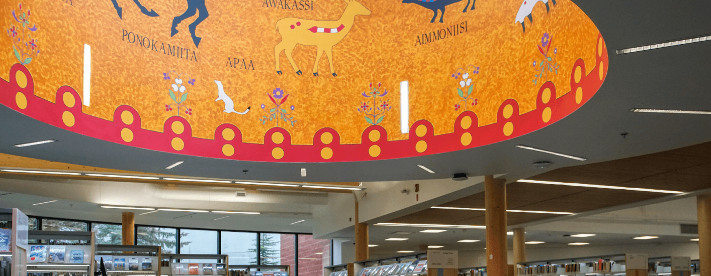 A vibrant ceiling mural depicts various animals, including a horse, deer, and sheep. The mural incorporate Indigenous words and artistic motifs.
