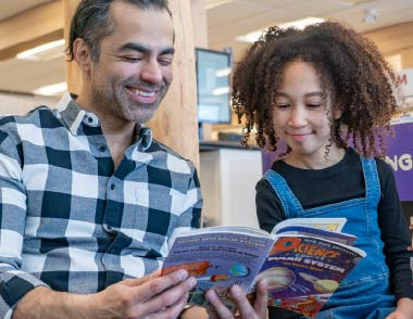 Adult and child reading a book together at the library.
