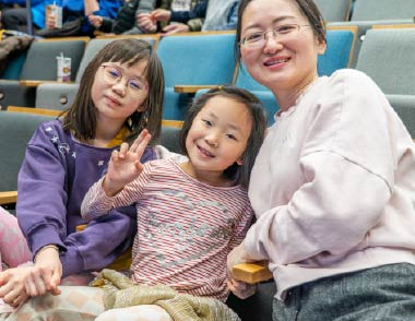 Two children and an adult seated together in a library audience.
