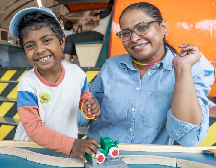 background image: Child and adult participating in a hands-on activity together at the library.