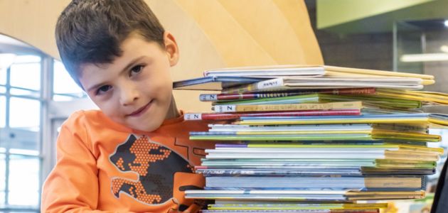 Child holding a tall stack of borrowed library books.