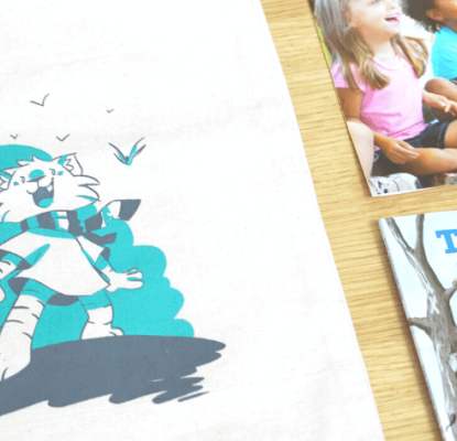 Photograph of a canvas book bag with an illustration of a cat and a book, the Calgary Public Library logo and text that reads "ready for kindergarten." There are also other reading materials on the table beside the bag. 
