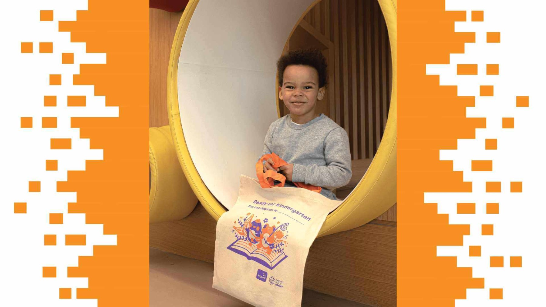 background image: This is a picture of a young child sitting in a pipe in the Early Learning Centre at Central Library. He is holding a tote bag that says "Ready for Kindergarten" and has a cute illustration of a frog and penguin standing on a book.