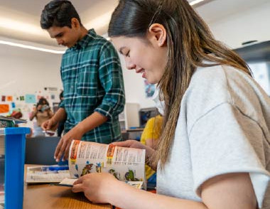 Teen reading a book while participating in a library activity.