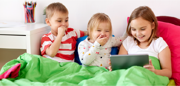 A picture of three kids laughing as they watch something on their tablet.