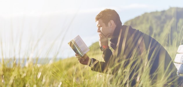 An image of a man sitting on a bench reading a book.