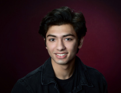 Rozsa Arts Musician Awab Paracha poses for a studio headshot against a dark red background.