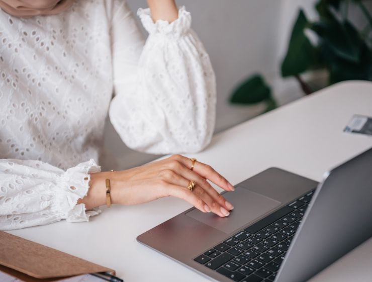 background image:  A woman in a white blouse sitting at a desk using a laptop.