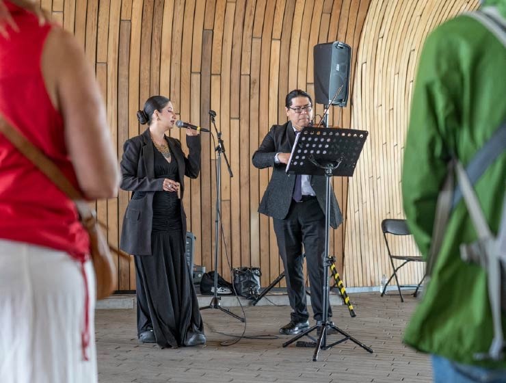background image: Musicians singing and playing music for an audience under the archway at Central Library. 