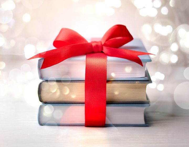 background image: Stack of three books tied with a bright red ribbon, set against a soft, glowing holiday background.