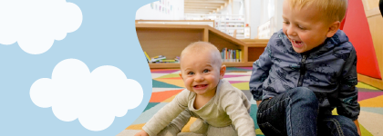 A toddler and a baby sitting on a mat at Central Library. 