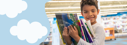 A young boy carrying a bunch of books and smiling at the camera