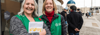 Two women standing outside Central Library wearing green vests.