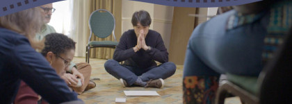 Participants sit in a circle on the floor during a group workshop activity, with cards and paper materials placed in the centre of the room.