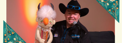 Indigenous Puppeteer DerRic Starlight, performs on stage with a handmade puppet beside a microphone.