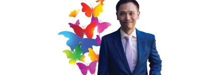 Person in a blue suit and tie standing next to colourful flying butterfly graphics used to promote the event Digital Decolonizing Transgender History The View from the Asia Pacific