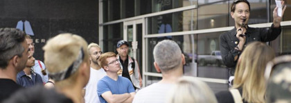 A tour guide leading a group of adults on a tour in front of a glass building.
