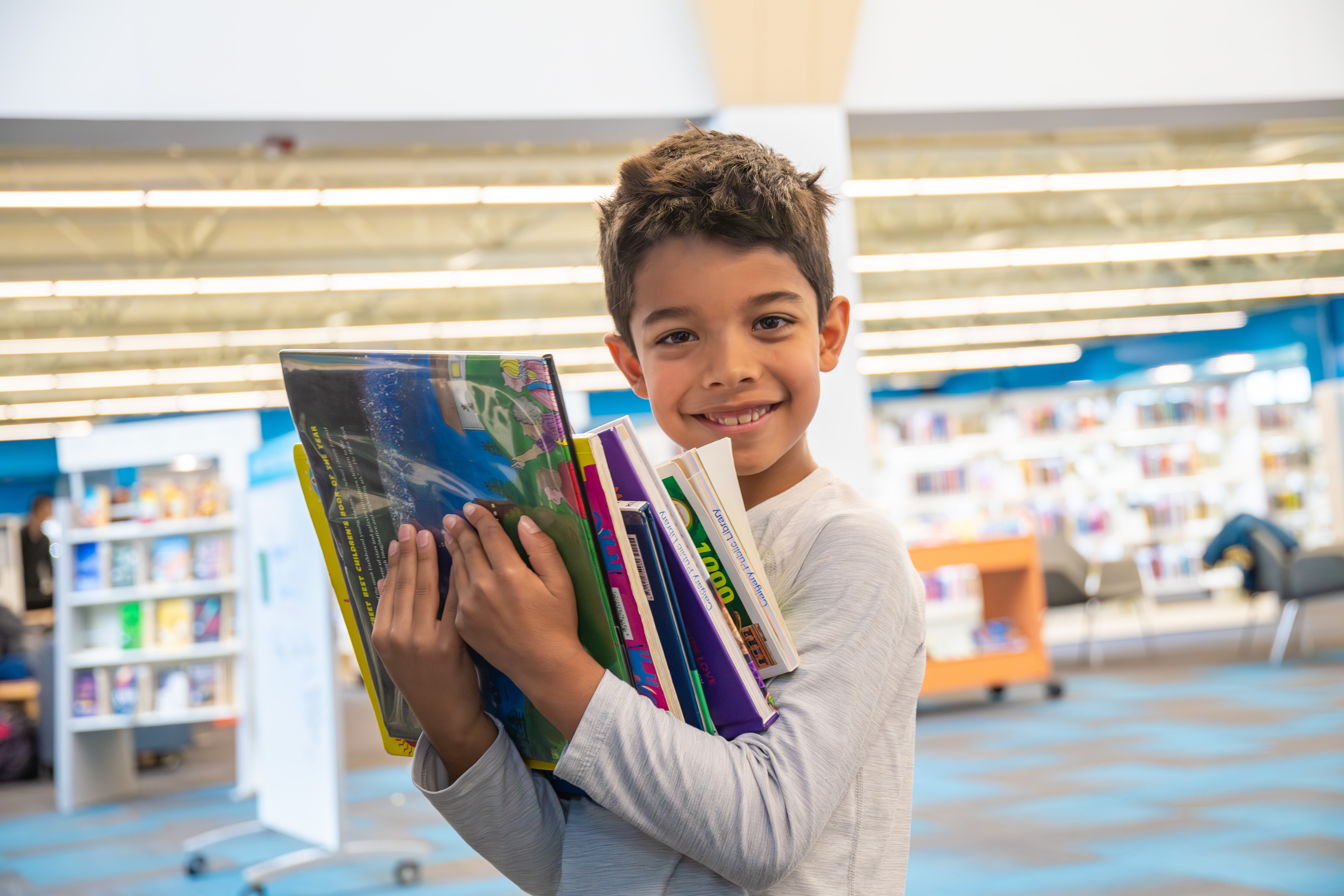 A young boy holds many books in his arms.