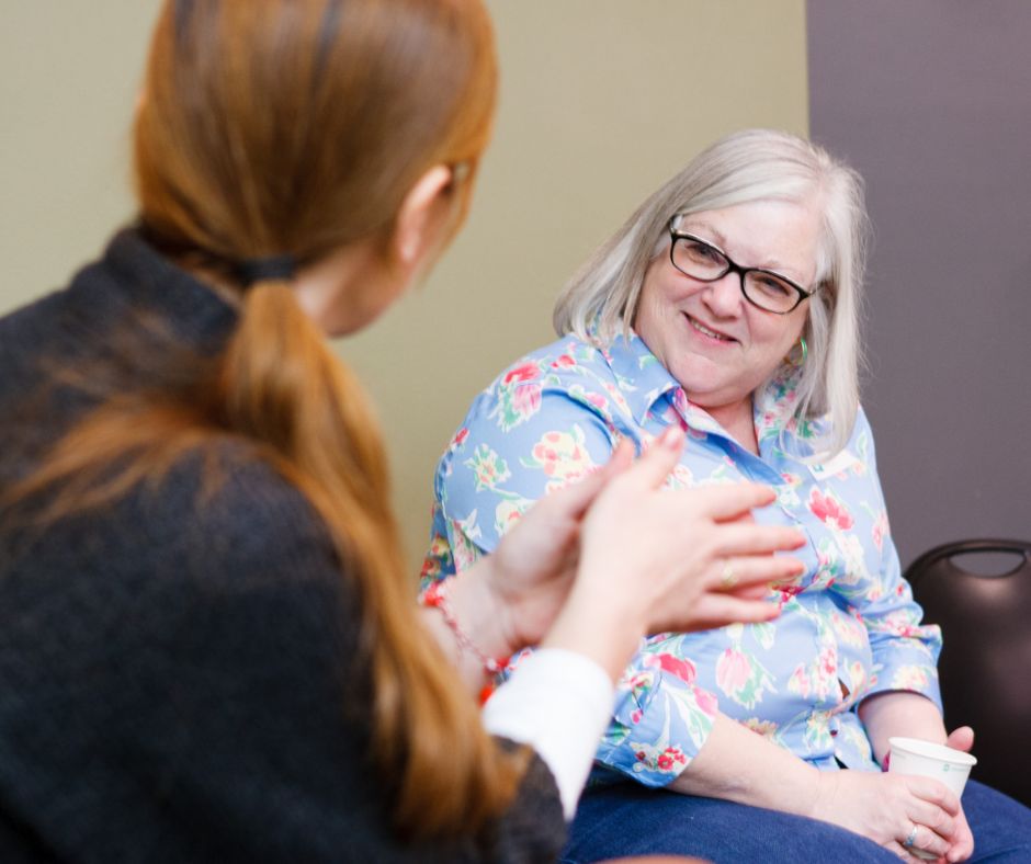 Two woman having a conversation. One is facing the other making a gesture.