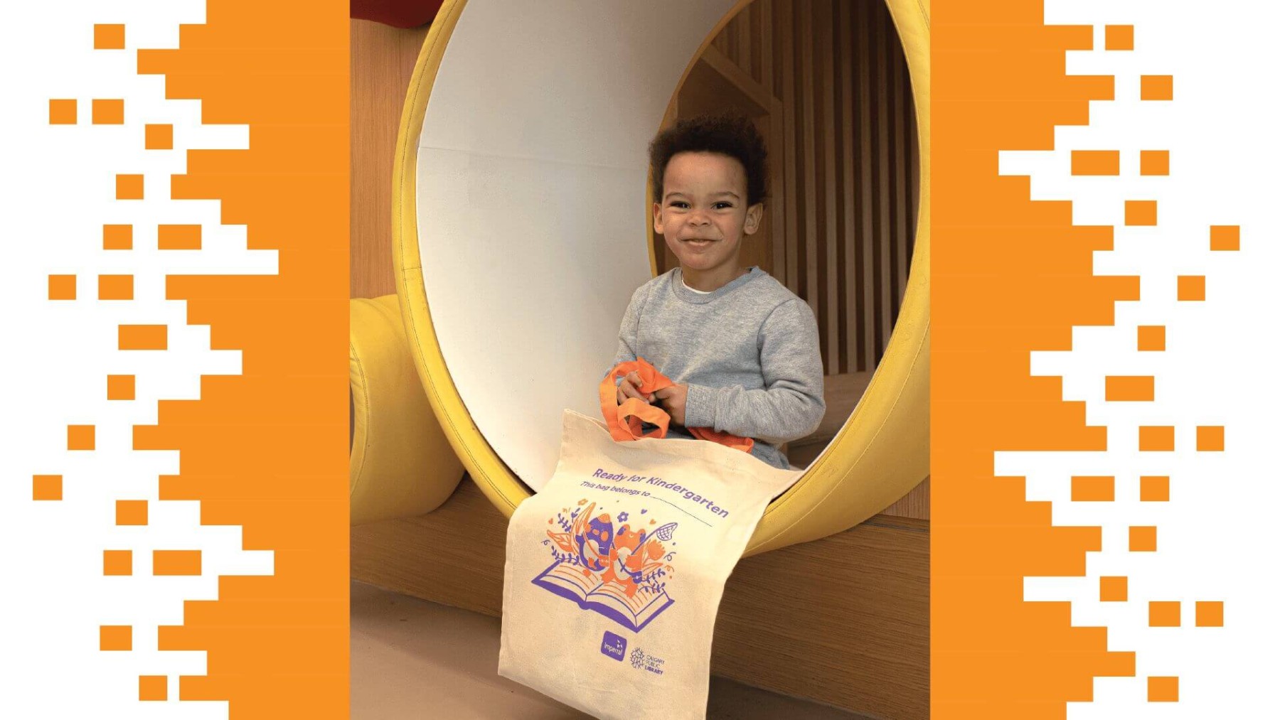 background image: This is a picture of a young child sitting in a pipe in the Early Learning Centre at Central Library. He is holding a tote bag that says "Ready for Kindergarten" and has a cute illustration of a frog and penguin standing on a book.