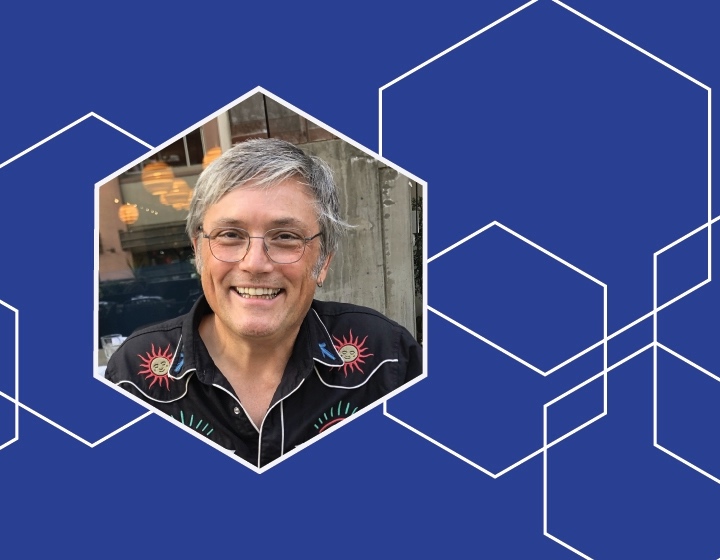 Headshot of 2026 Creative in Residence AIC Paul Freeman surrounded by a blue border with white geometric pattern.