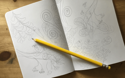 A photo of a notebook with pencil scribbled drawings on top of it. There is a diagonal yellow pencil on top of it.