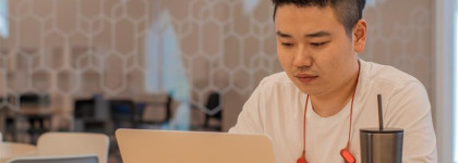 A photograph of an adult sitting at a table and typing on a computer. 