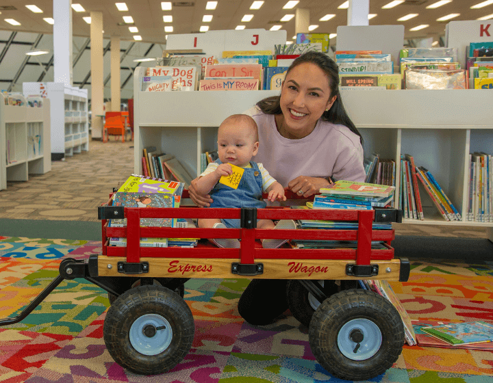 background image: A woman kneeling beside a wagon which contains a baby and books.