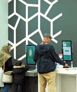 People at a library borrowing books using a self checkout machine.