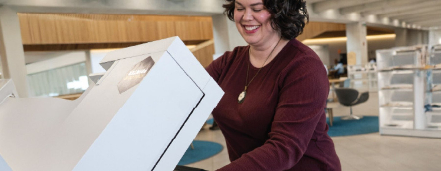 A smiling person returns books at a self-service return station inside a library.