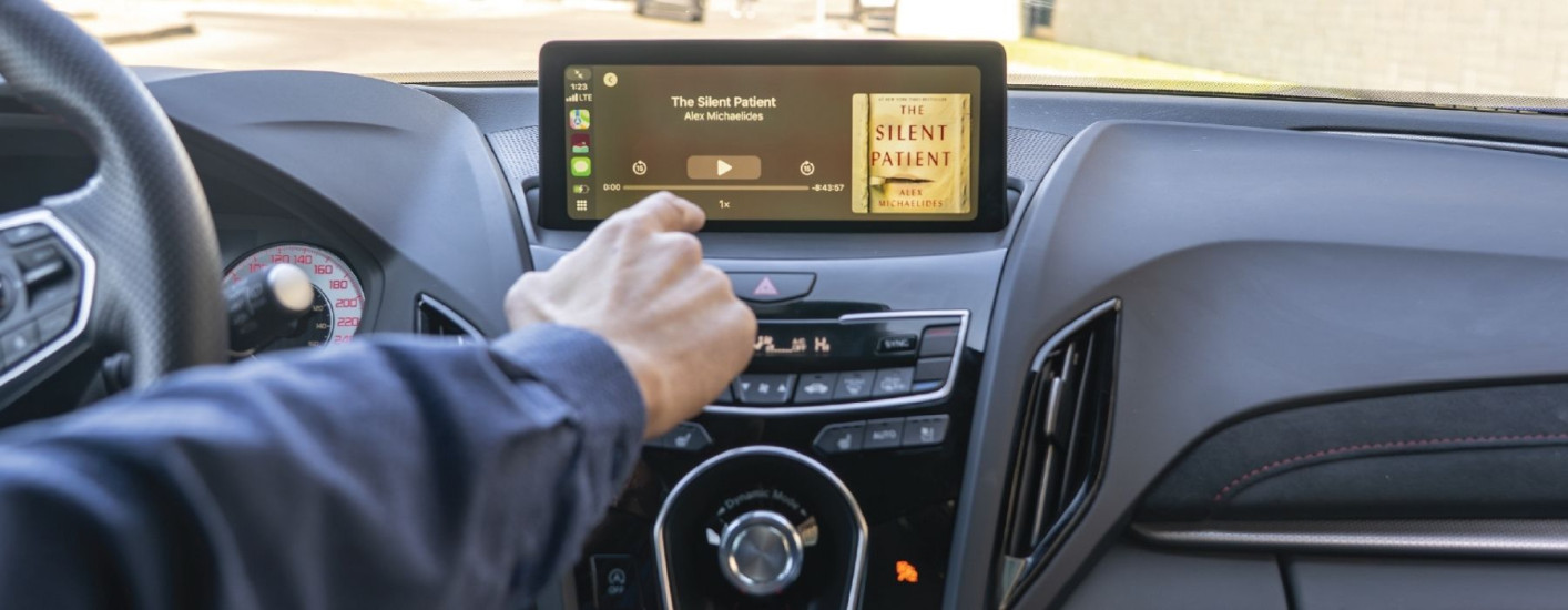 A person sits in a car listening to the audiobook “The Silent Patient” displayed on the dashboard screen.