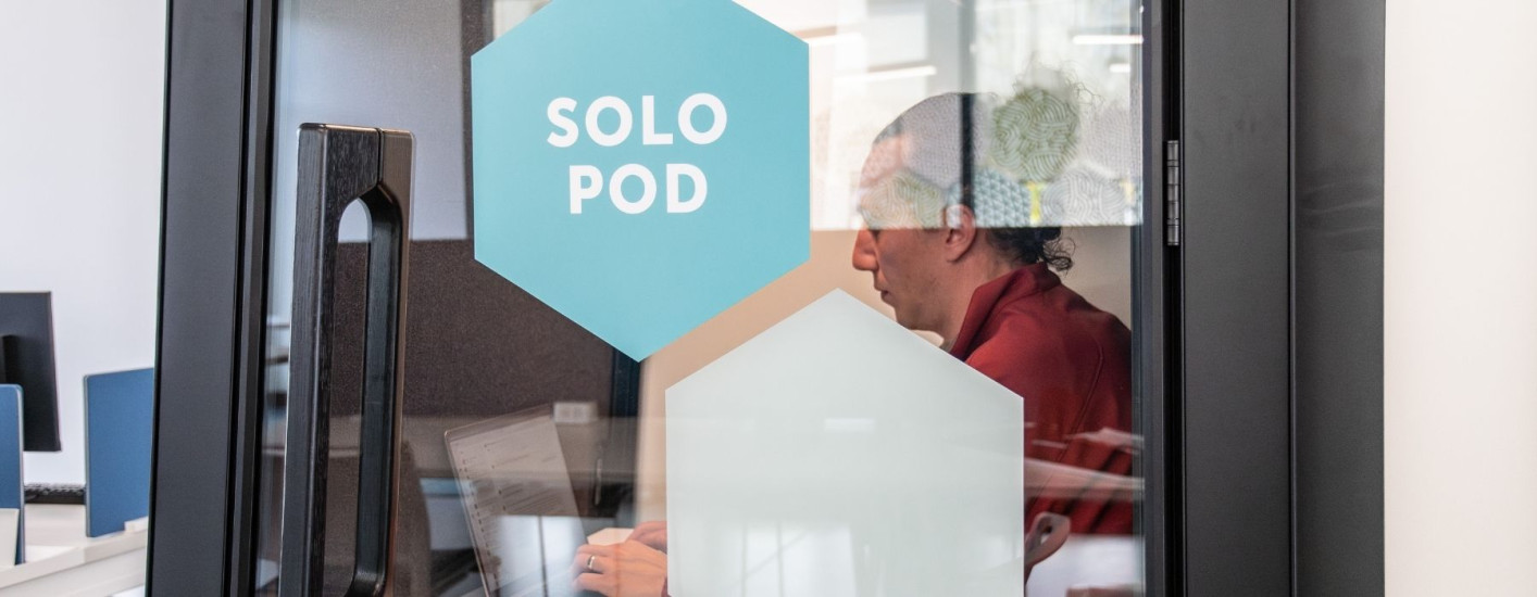 Signage that says Solo Pod and within the cubicle there is a person working on a computer.